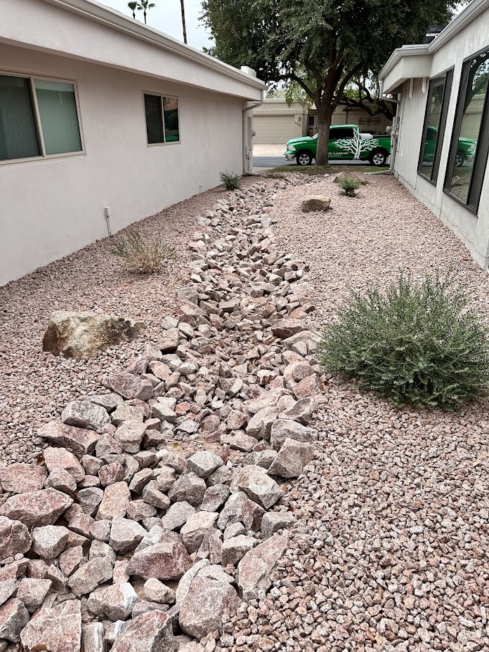Rocky dry creek between houses and shrubs.