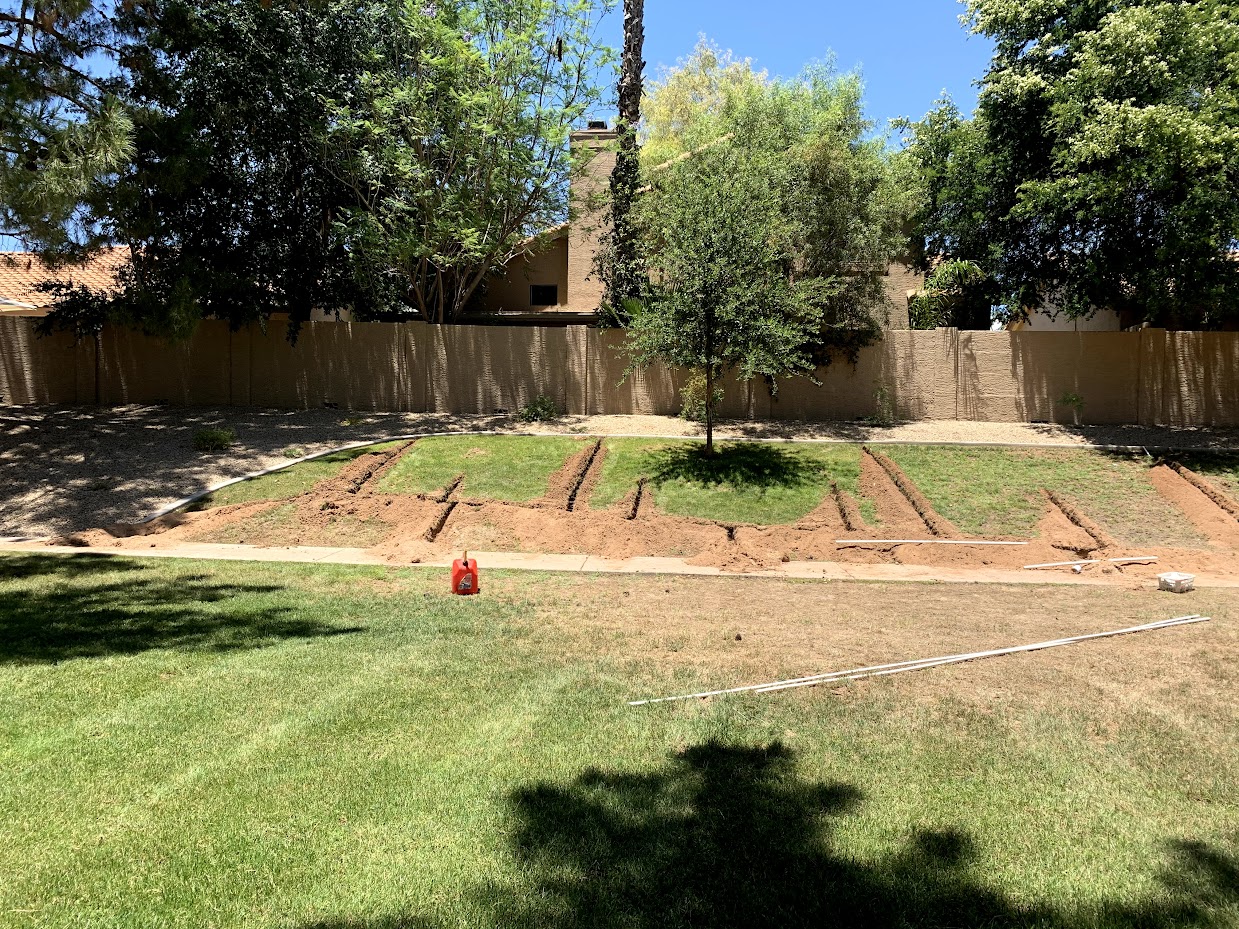 Backyard with lawn, trees, and soil preparation for planting.