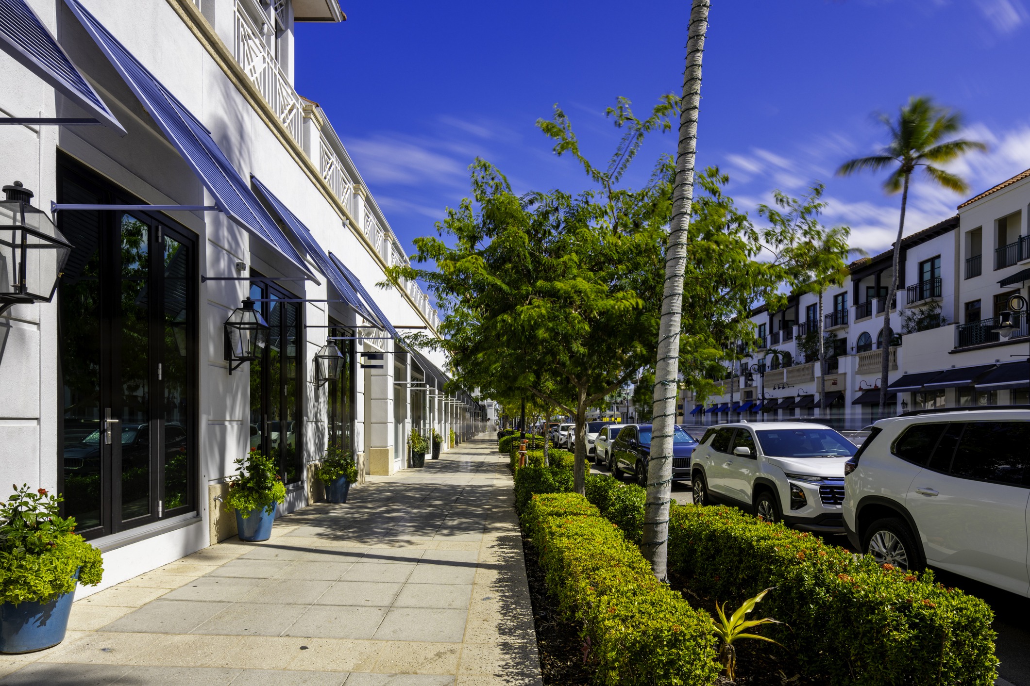 Sunny street with cars and shops.