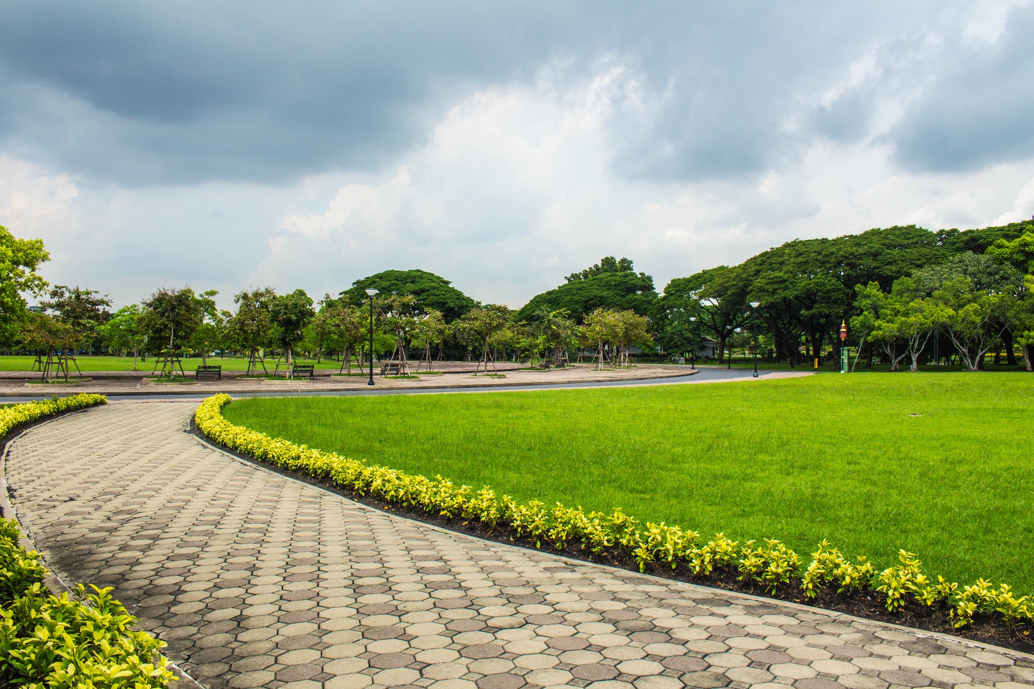 Curved pathway through green park with cloudy sky.