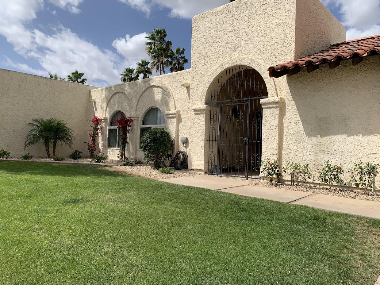 Spanish-style stucco home with arched entryway, wrought iron gate, and bougainvillea