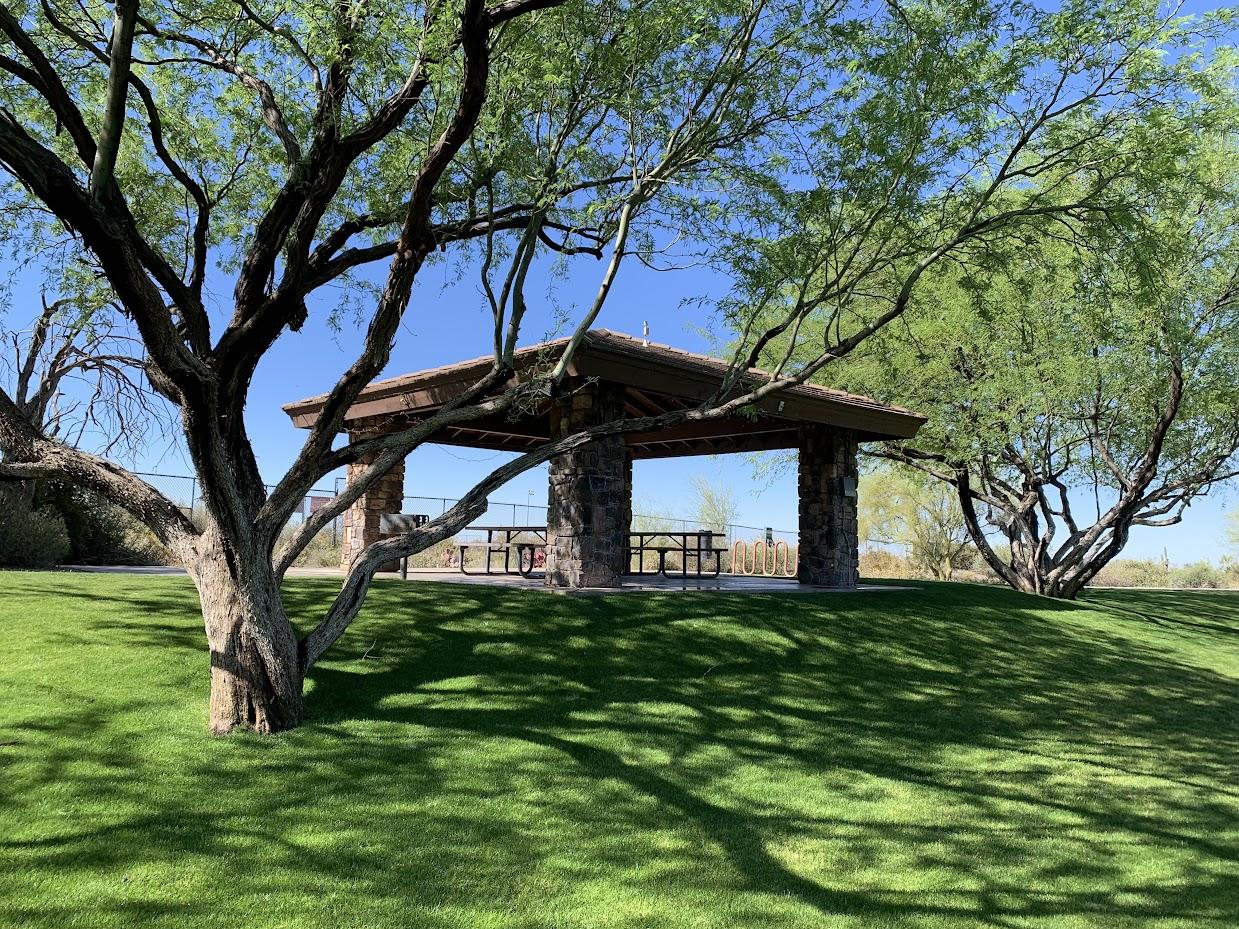 Stone ramada with picnic tables on a green lawn in an Arizona park